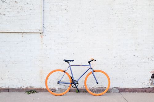 Orange and purple bike leaning against a white brick wall